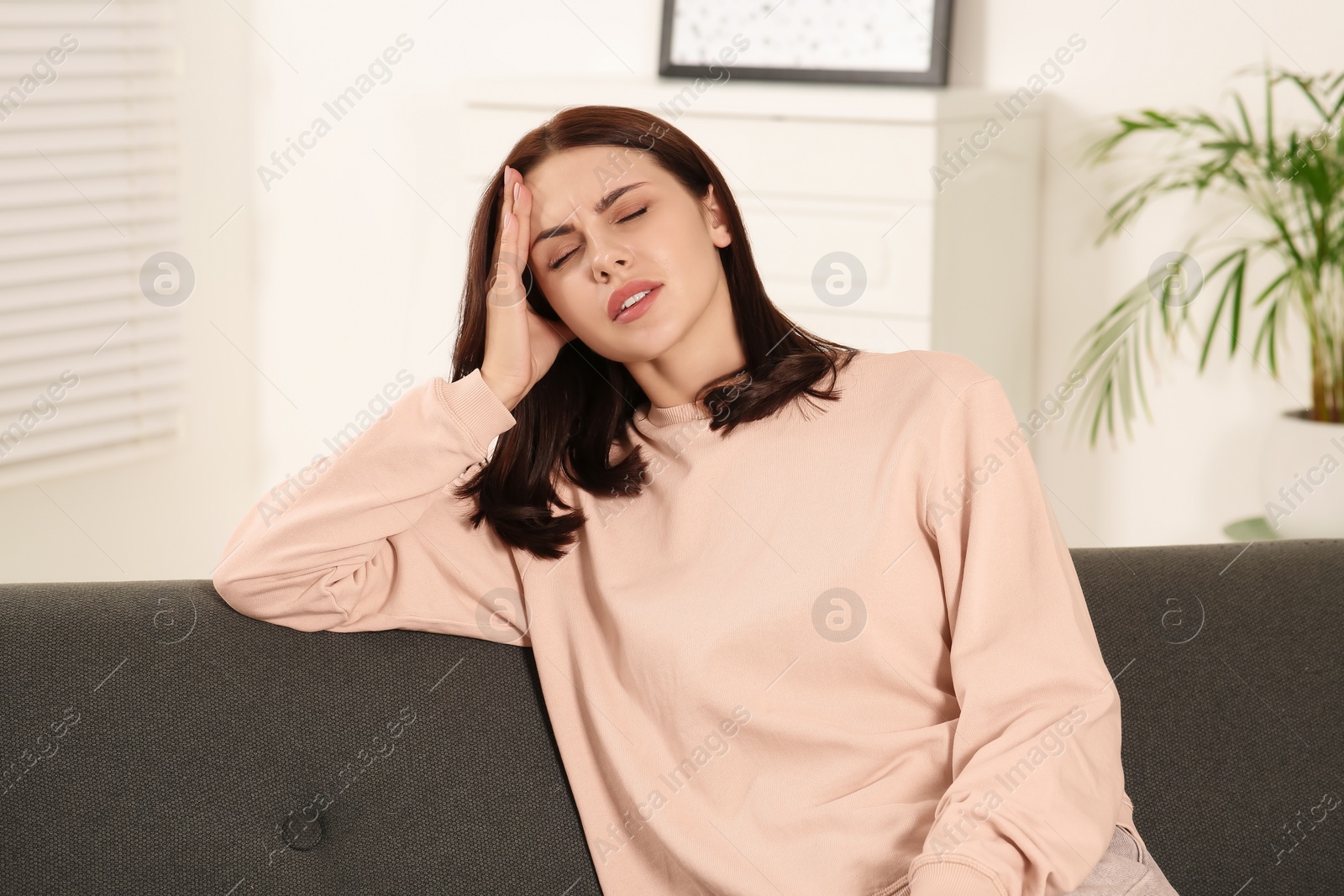 Photo of Young woman suffering from headache indoors. Hormonal disorders