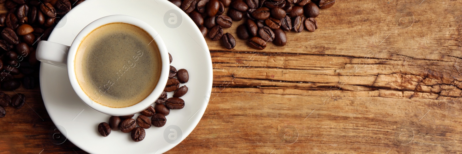 Image of Cup of hot aromatic coffee and roasted beans on wooden table, top view with space for text. Banner design