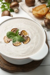 Photo of Fresh homemade mushroom soup in ceramic pot on white wooden table, closeup