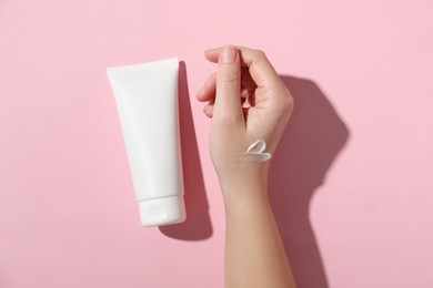 Photo of Woman with tube of hand cream on pink background, top view