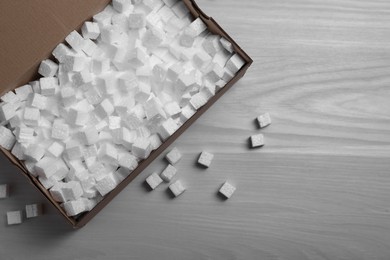 Photo of Cardboard box and styrofoam cubes on wooden floor, flat lay. Space for text