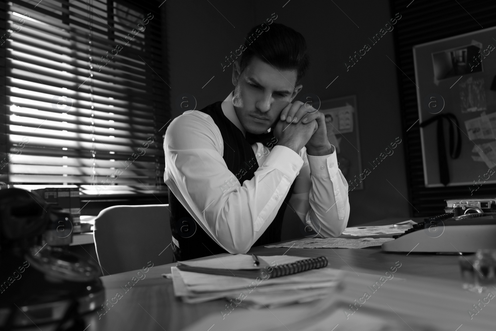 Photo of Old fashioned detective working at table in office. Black and white effect