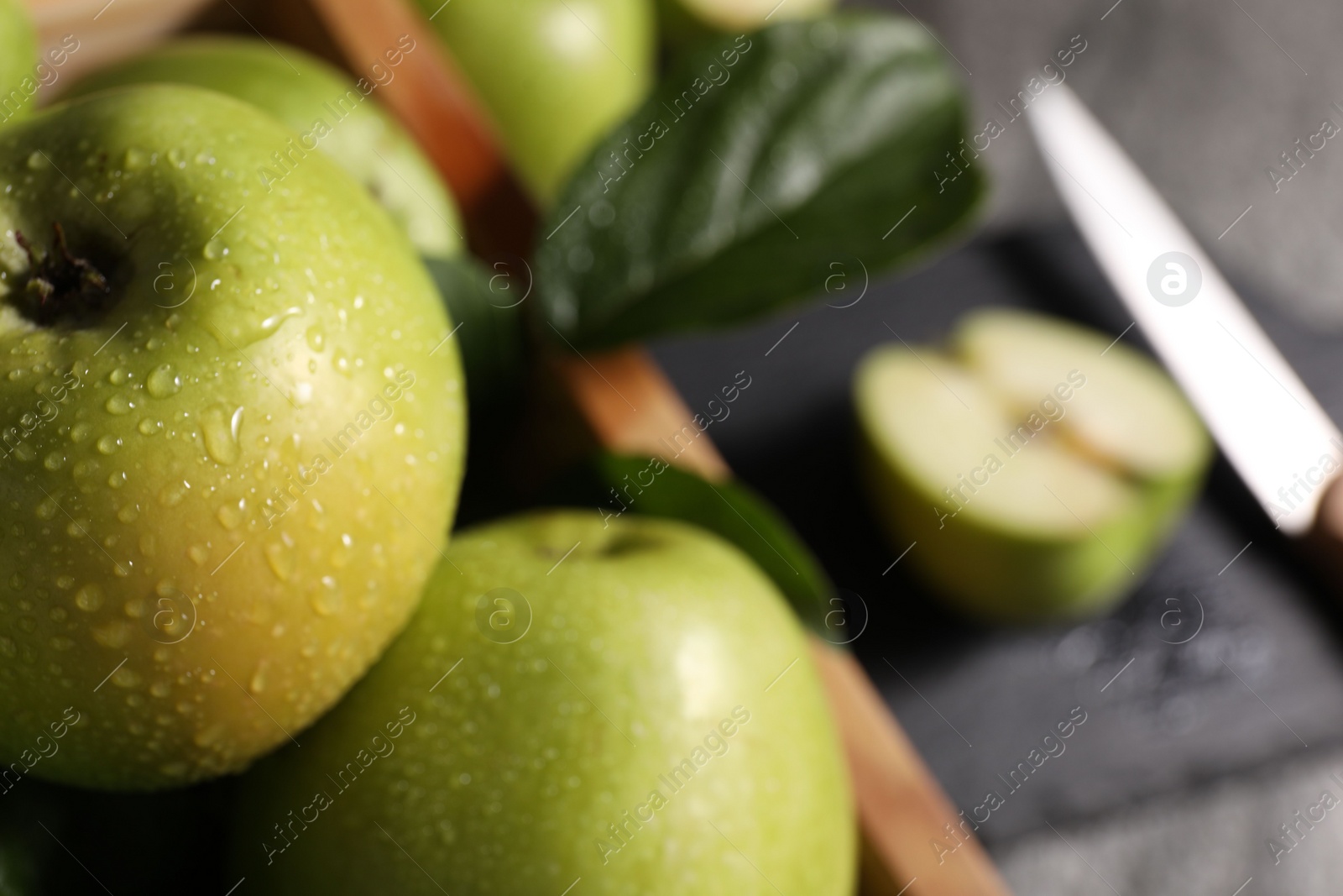 Photo of Ripe green apples with water drops in crate on table, closeup. Space for text