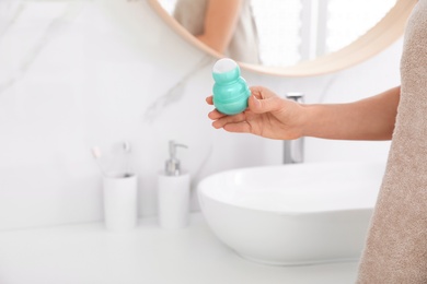 Young woman with roll on deodorant in bathroom, closeup view. Space for text