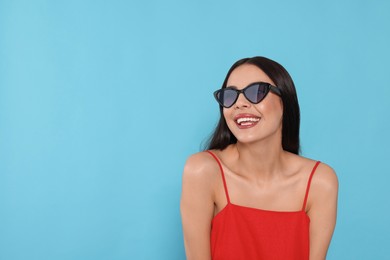 Photo of Attractive happy woman in fashionable sunglasses against light blue background. Space for text