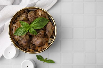 Photo of Delicious fried chicken liver with onion and basil in bowl on white tiled table, flat lay. Space for text