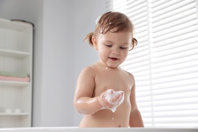 Photo of Cute little girl playing with foam in bathtub at home
