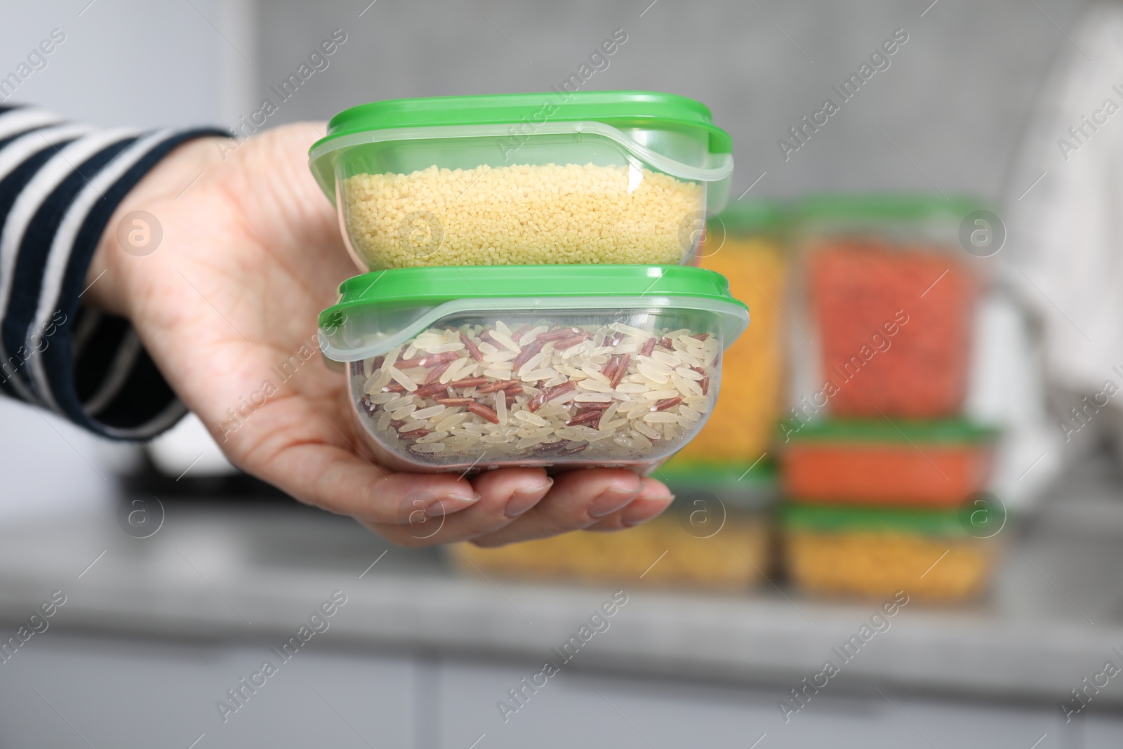 Photo of Woman holding plastic containers of raw couscous and rice indoors, closeup with space for text. Food storage