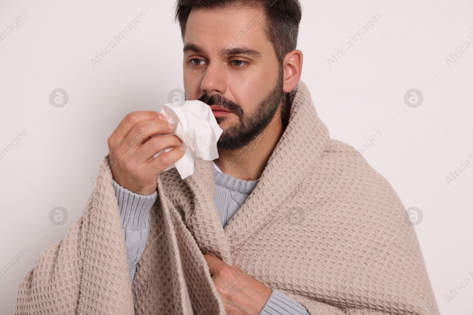 Photo of Sick man wrapped in blanket with tissue on light grey background. Cold symptoms