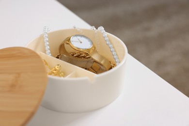 Photo of Jewelry box with wristwatch and accessories on white table, closeup