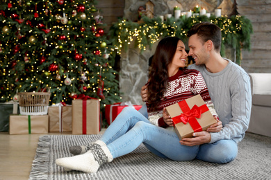 Photo of Happy couple with gift box in living room decorated for Christmas