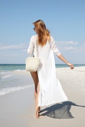 Beautiful woman with beach bag walking near sea, back view