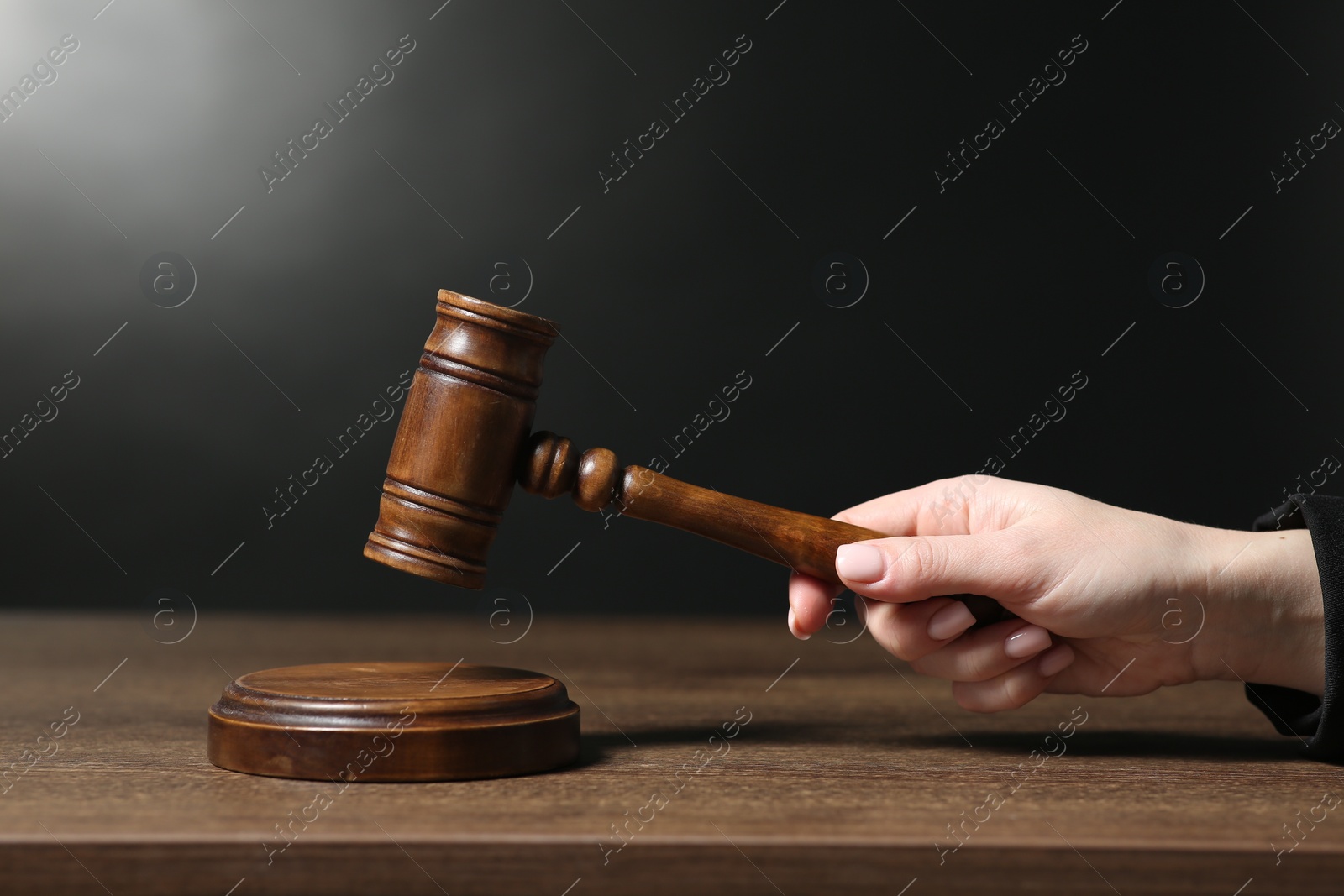 Photo of Judge striking mallet at wooden table against dark background, closeup