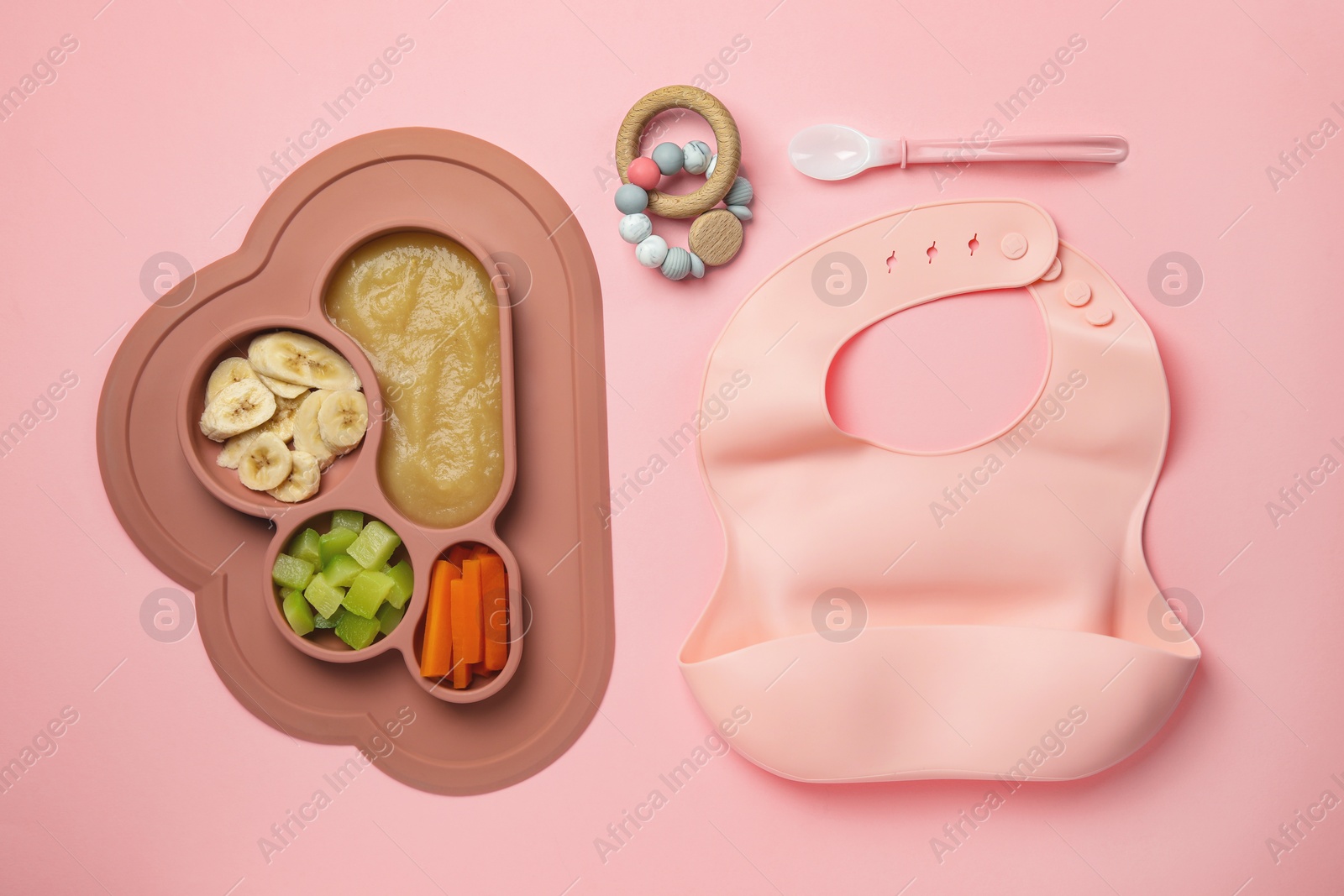 Photo of Section plate with healthy baby food, toy and bib on pink background, flat lay