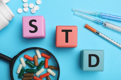 Photo of Abbreviation STD made with cubes near different drugs on light blue background, flat lay