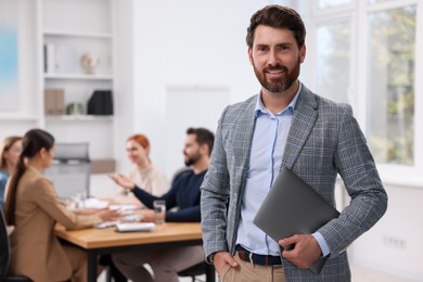 Photo of Team of employees working together in office. Stylish businessman with laptop indoors