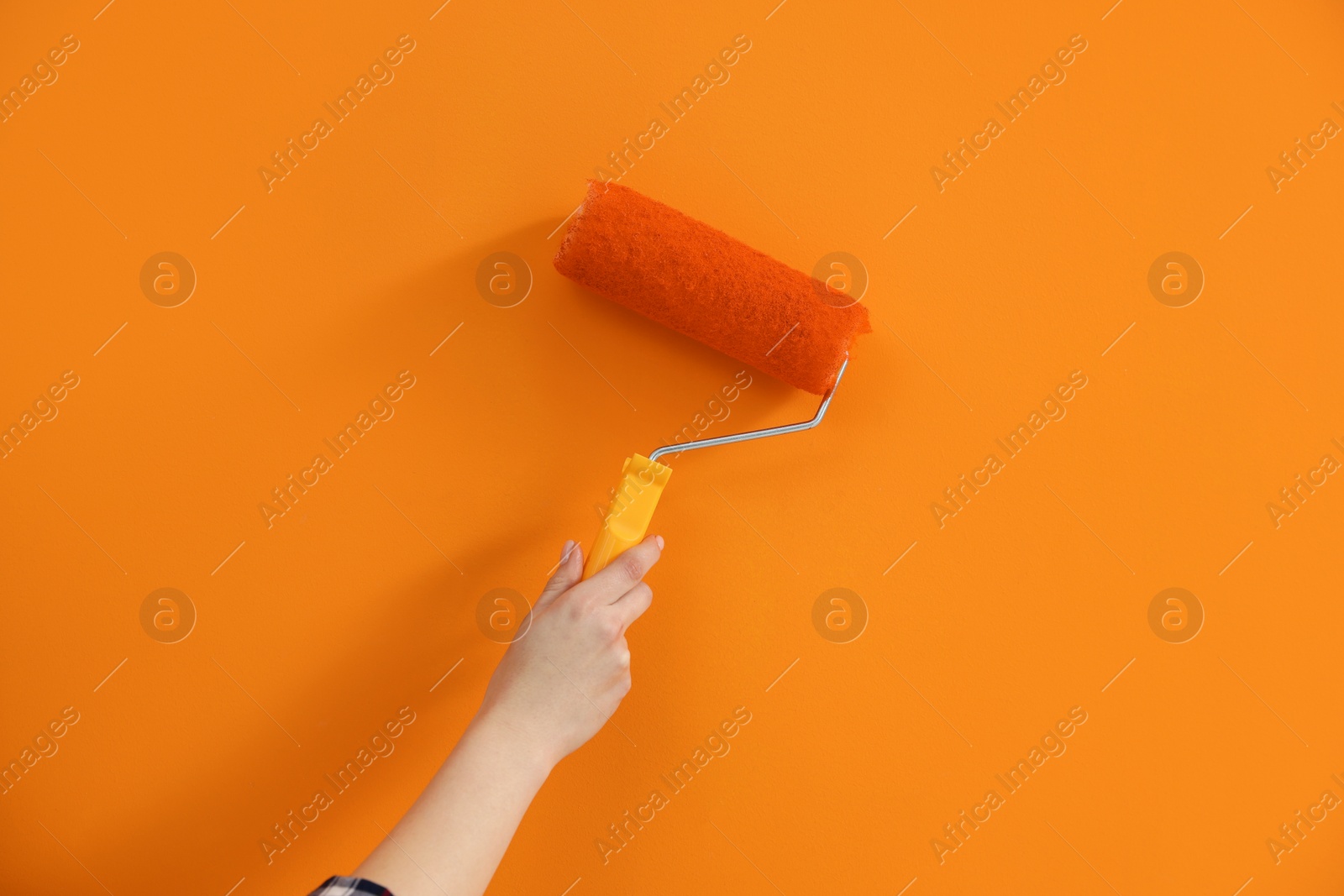 Photo of Designer painting orange wall with roller, closeup