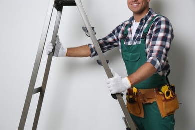 Photo of Professional builder with metal ladder on light background, closeup
