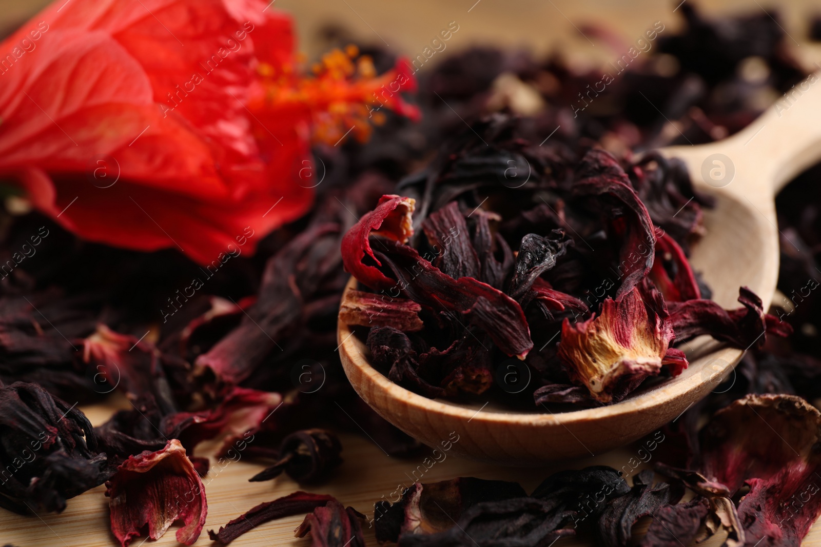 Photo of Wooden spoon with dry hibiscus tea on table, closeup