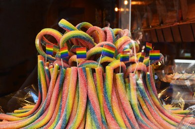 Photo of Delicious gummy candies and many bright rainbow LGBT pride flags in shop