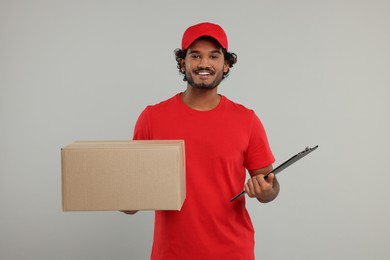 Happy courier with parcel and clipboard on grey background