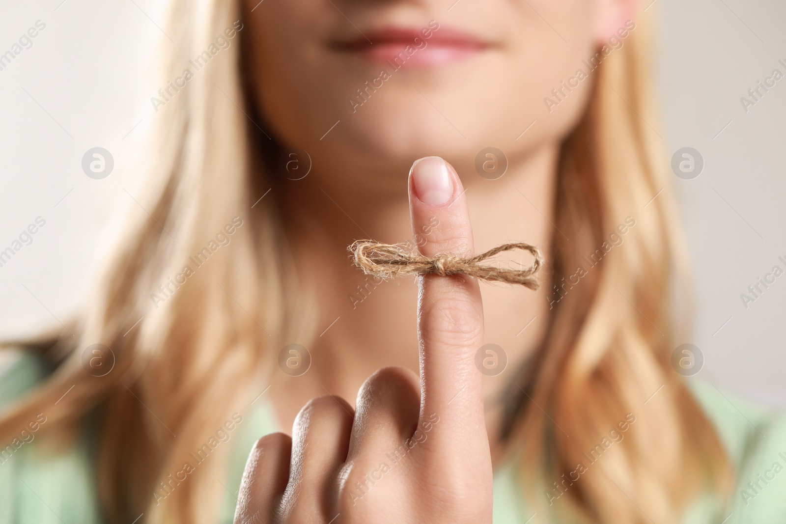 Photo of Woman showing index finger with tied bow as reminder against blurred background, focus on hand