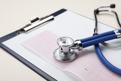 Photo of Stethoscope, clipboard and cardiogram paper on beige background, closeup