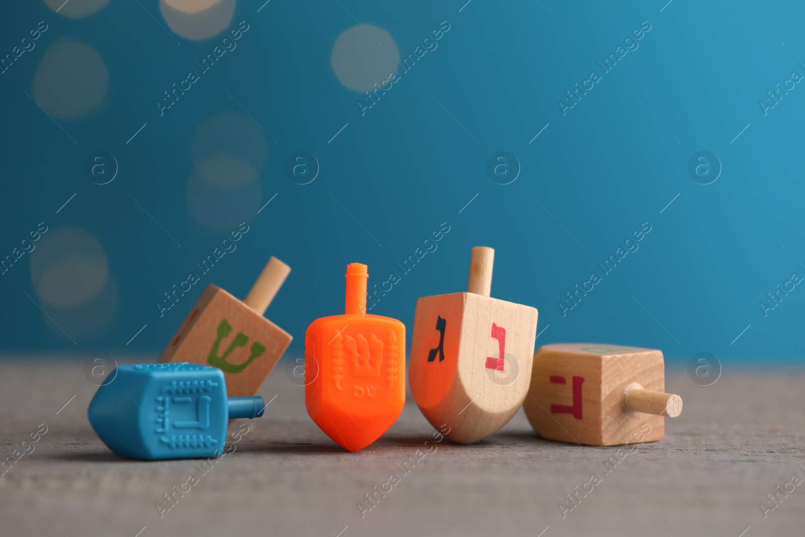 Photo of Different dreidels on wooden table against light blue background with blurred lights, space for text. Traditional Hanukkah game