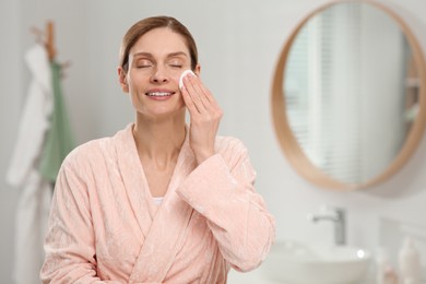 Photo of Beautiful woman removing makeup with cotton pad indoors, space for text