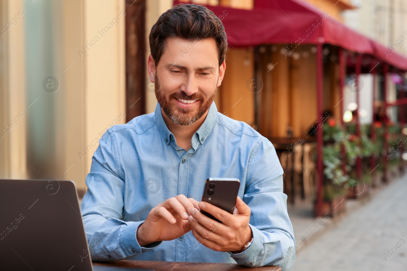 Photo of Handsome man using smartphone at table in outdoor cafe