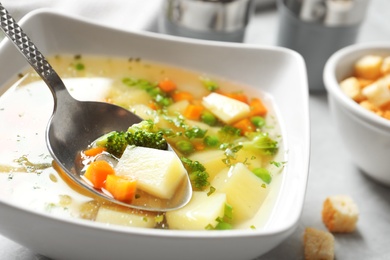 Photo of Spoon of fresh homemade vegetable soup over full bowl on table, closeup