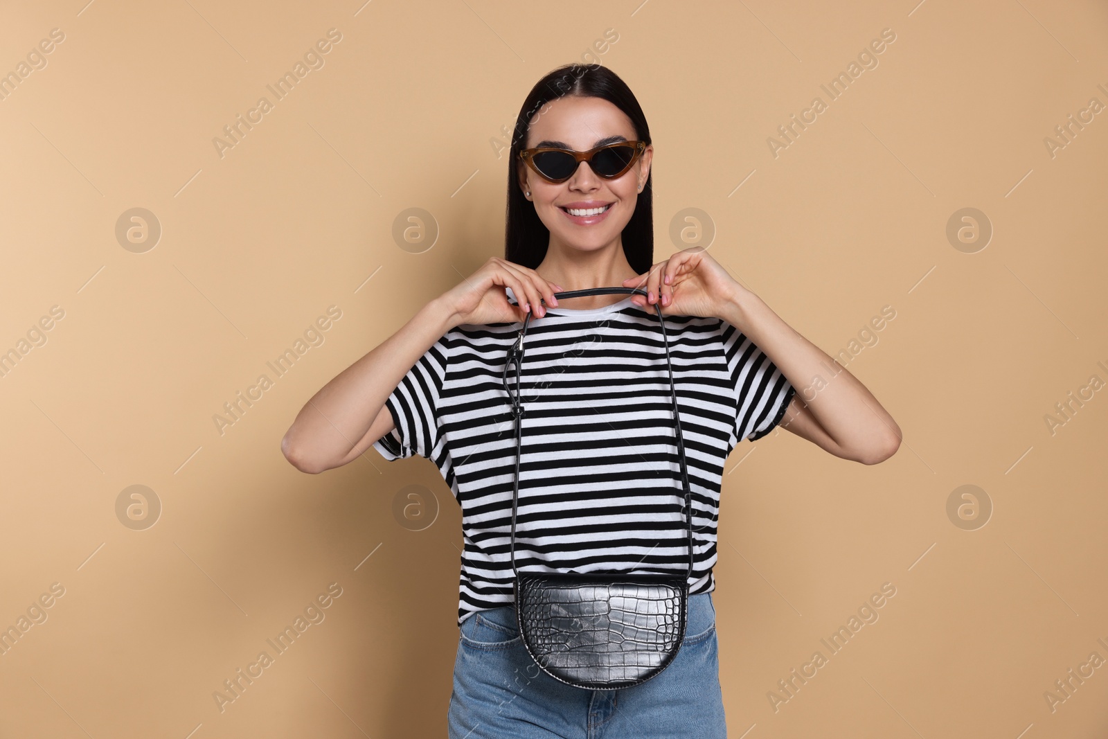 Photo of Beautiful young woman with stylish bag in sunglasses on beige background