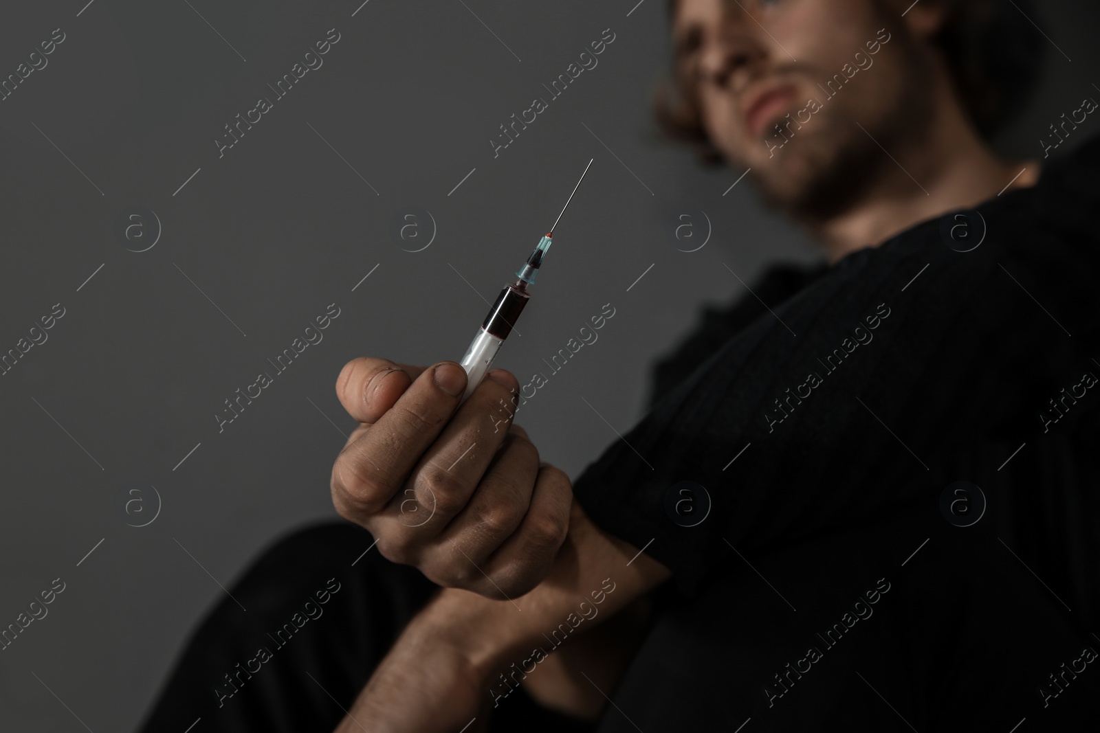 Photo of Young drug addict with syringe on grey background, closeup