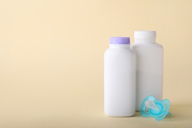 Photo of Baby powder in bottles and pacifier on beige background, space for text