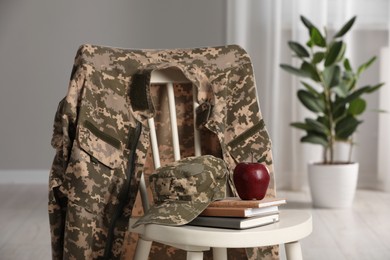 Photo of Chair with soldier uniform, notebooks and apple indoors. Military education