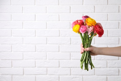 Photo of Woman holding beautiful ranunculus flowers near white brick wall, closeup. Space for text