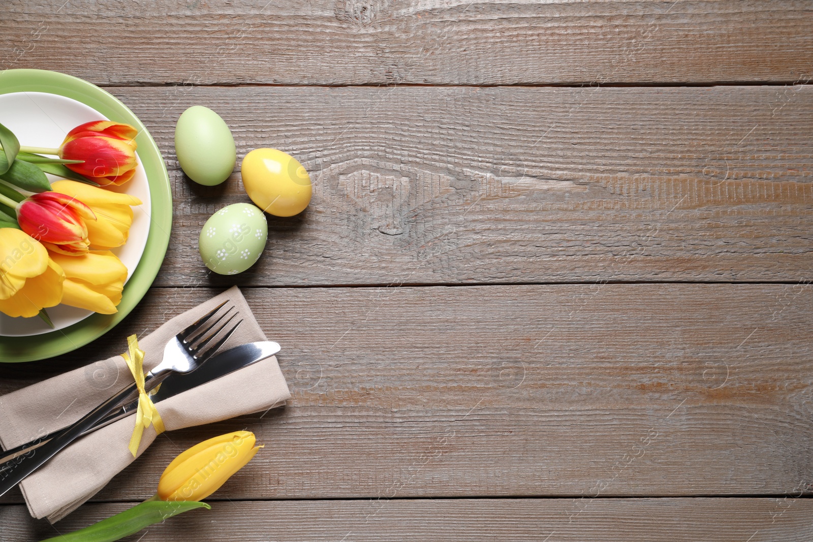 Photo of Festive Easter table setting with painted eggs and flowers on wooden background, flat lay. Space for text