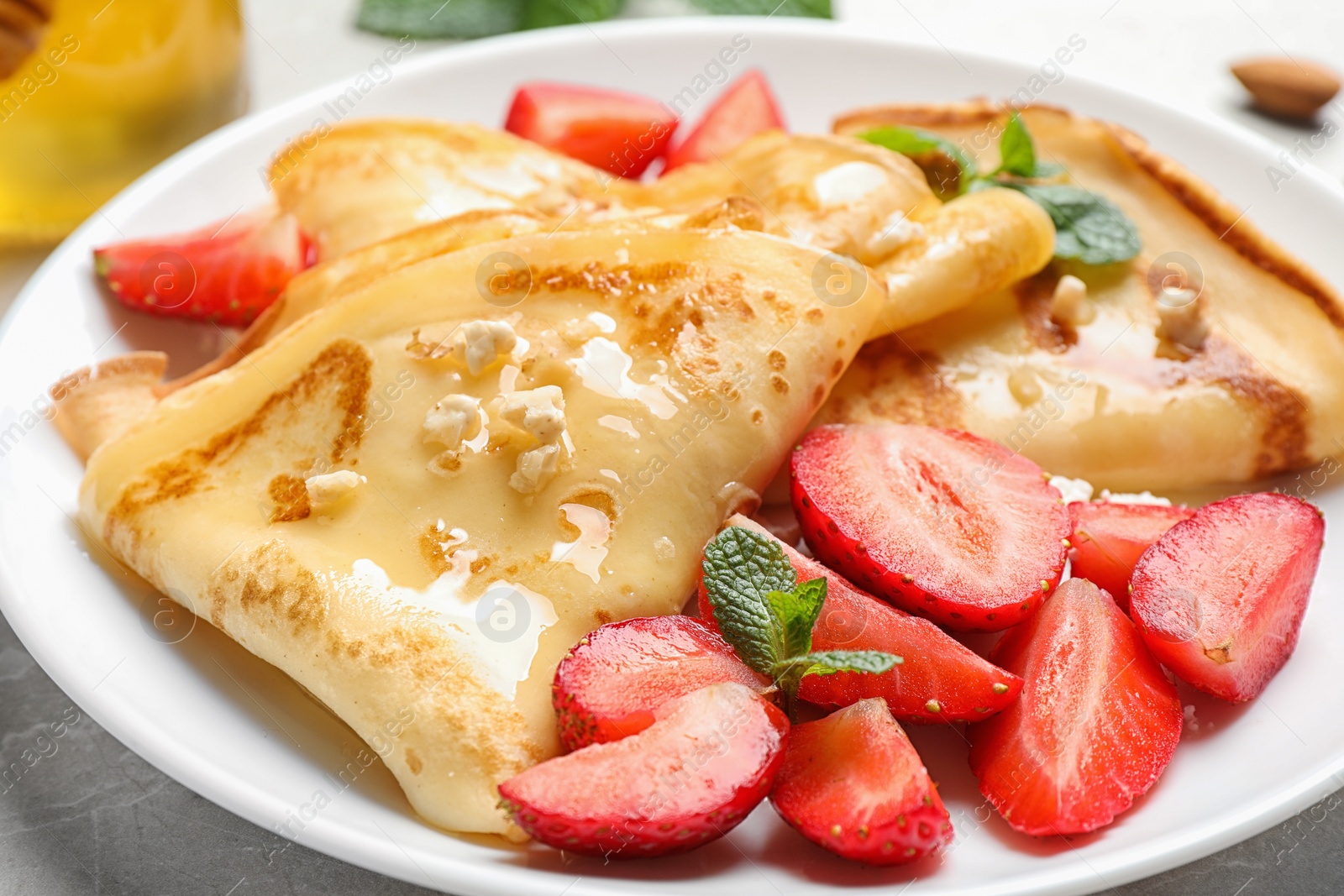 Photo of Delicious thin pancakes with strawberries, cottage cheese and honey on light table, closeup