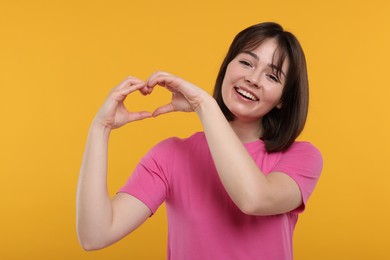 Photo of Happy woman showing heart gesture with hands on orange background