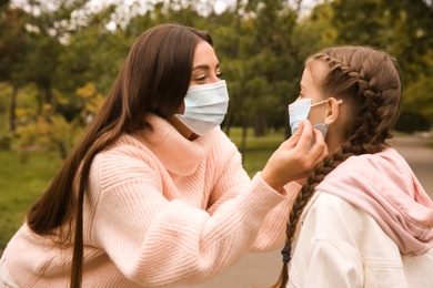 Mother putting mask onto face of little daughter in park during coronavirus pandemic