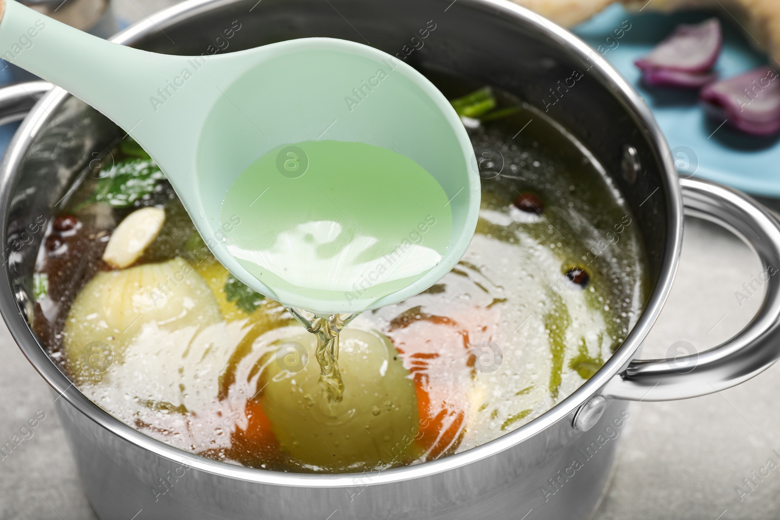 Photo of Ladle with tasty bouillon above pot at grey table, closeup