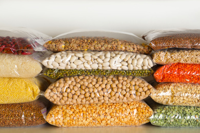 Photo of Different types of legumes and cereals in plastic bags on table. Organic grains