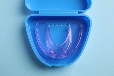 Container with dental mouth guard on light blue background, top view. Bite correction