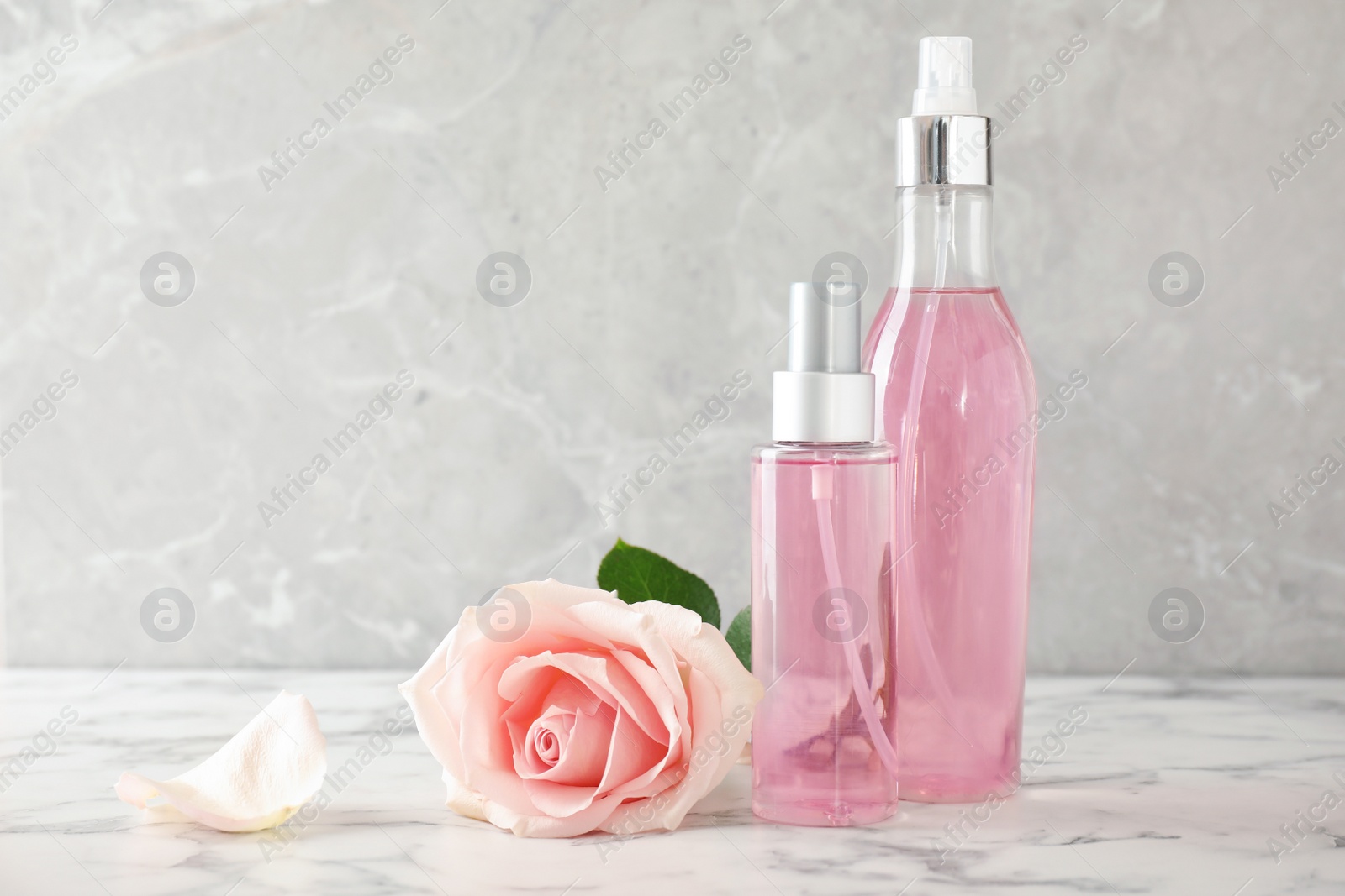 Photo of Bottles of essential oil and rose on marble table. Space for text