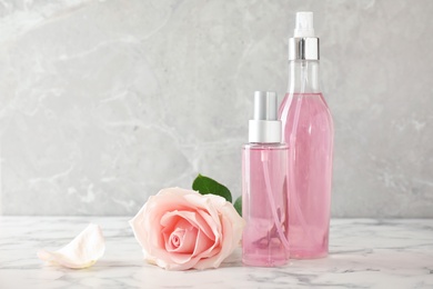 Bottles of essential oil and rose on marble table. Space for text