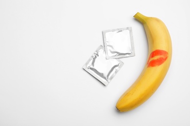 Photo of Condoms and banana with lipstick kiss mark on white background, top view. Safe sex