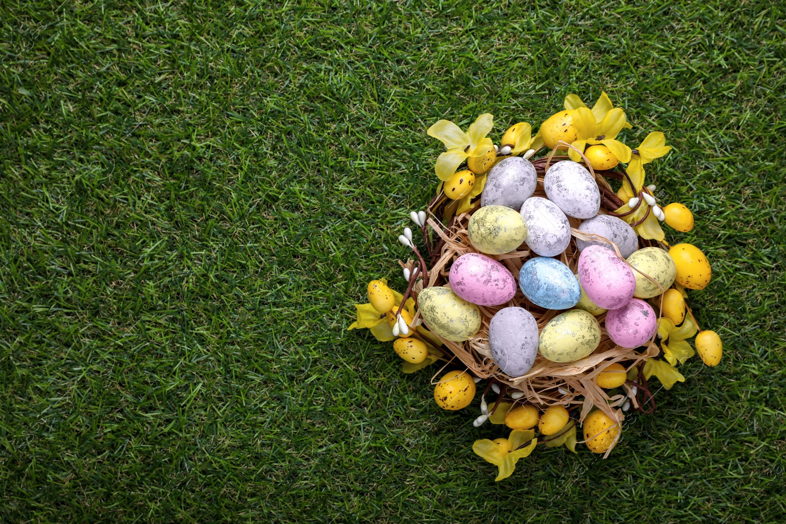 Photo of Festively decorated Easter eggs on green grass, top view. Space for text