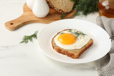 Photo of Plate with tasty fried egg, slice of bread and dill on white marble table