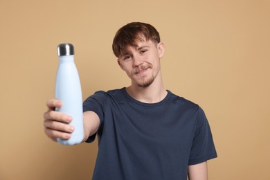 Happy man holding thermo bottle with drink on beige background