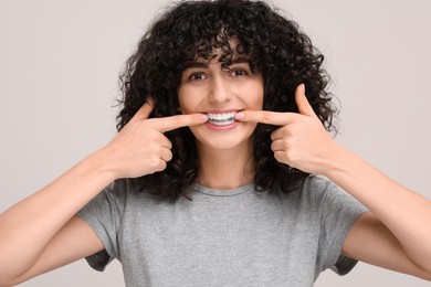 Photo of Young woman applying whitening strip on her teeth against light grey background